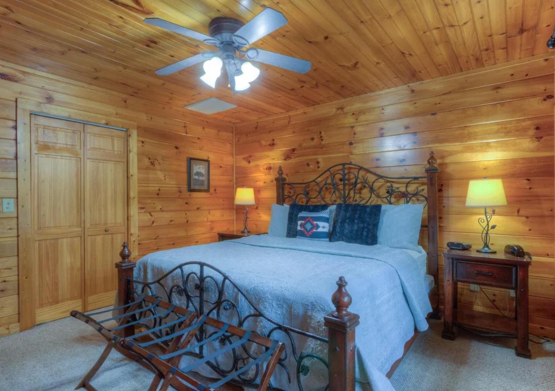 Sink into the inviting king bed surrounded by warm wood-paneled walls, soft lamplight, and a gentle ceiling fan overhead—your cozy mountain retreat awaits.