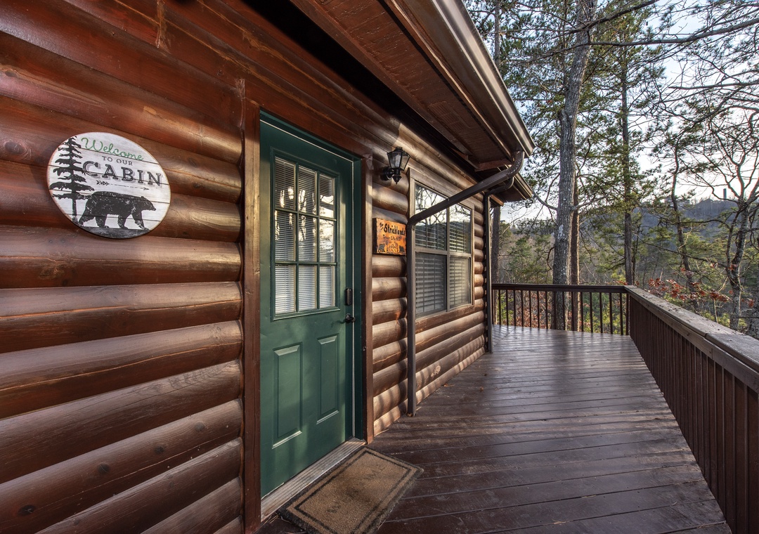 Rustic log cabin entrance with charming green door and wraparound deck nestled among towering trees.