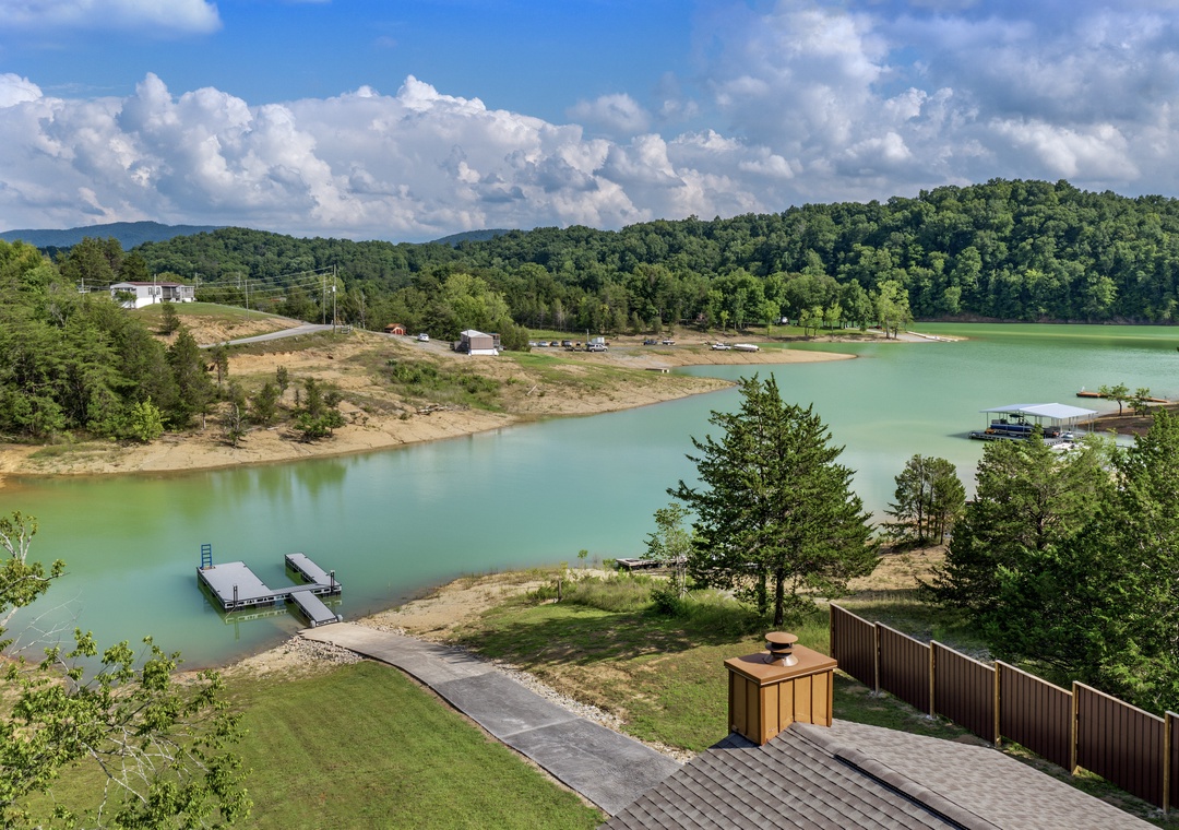 Aerial view of the property's private lakefront setting, with docks, lush forested hills, and open skies framing the tranquil waterfront location.