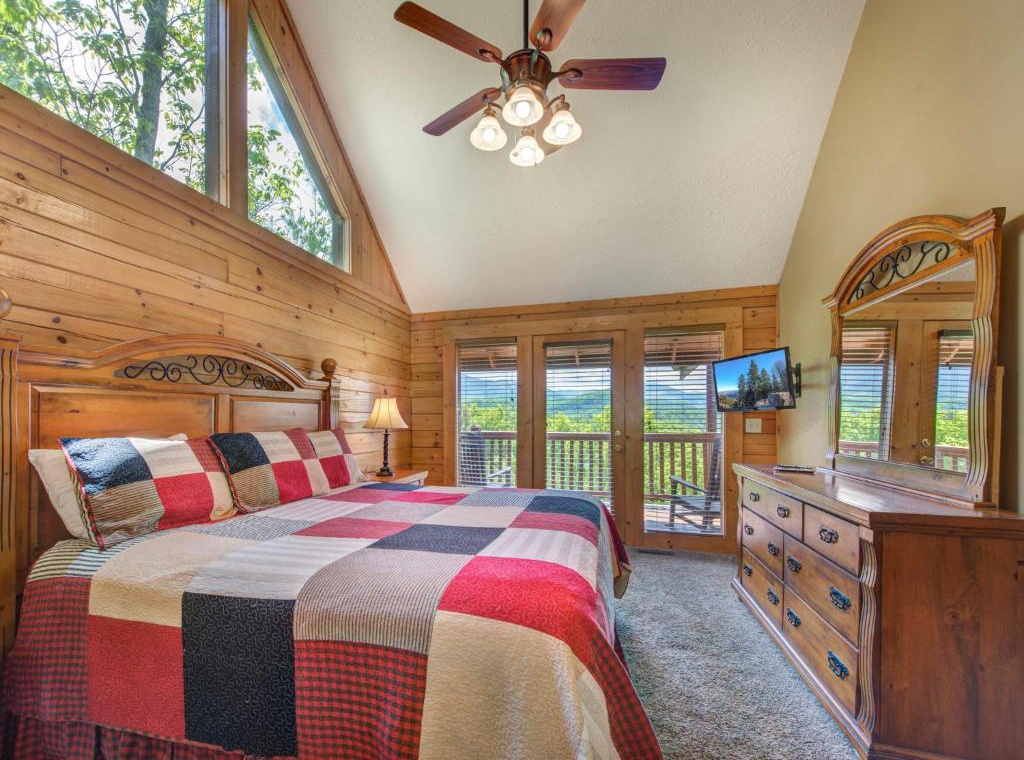 Unwind in your cozy cabin bedroom with rustic wood walls, cheerful quilt bedding, and private balcony access to stunning valley views.