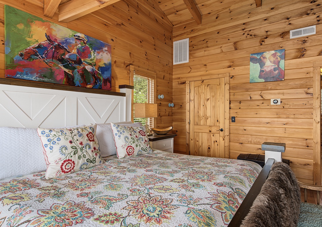 Cozy up in your rustic wood-paneled bedroom featuring a plush bed with vibrant linens, unique artwork, and warm cabin charm—your peaceful mountain retreat awaits.