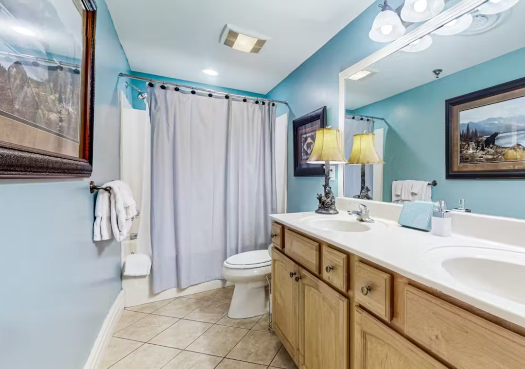 Your spacious bathroom features warm wood vanity, dual sinks, and relaxing tub-shower combo in soothing blue tones.