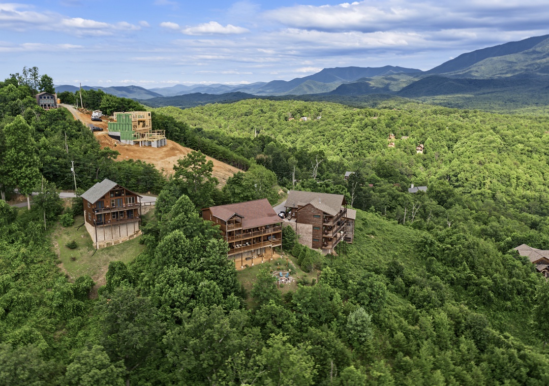 Aerial view of mountain properties nestled among lush forests with expansive mountain ranges stretching across the horizon under a cloudy sky.