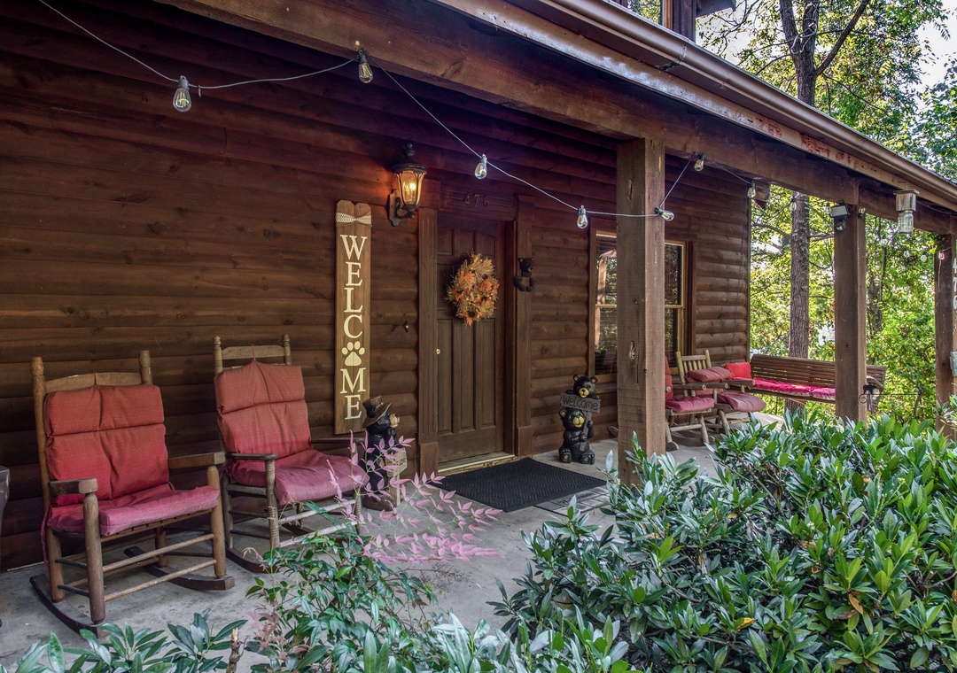 The charming front porch welcomes you to this peaceful woodland retreat, where rustic wooden rocking chairs and lush greenery invite you to relax and unwind.
