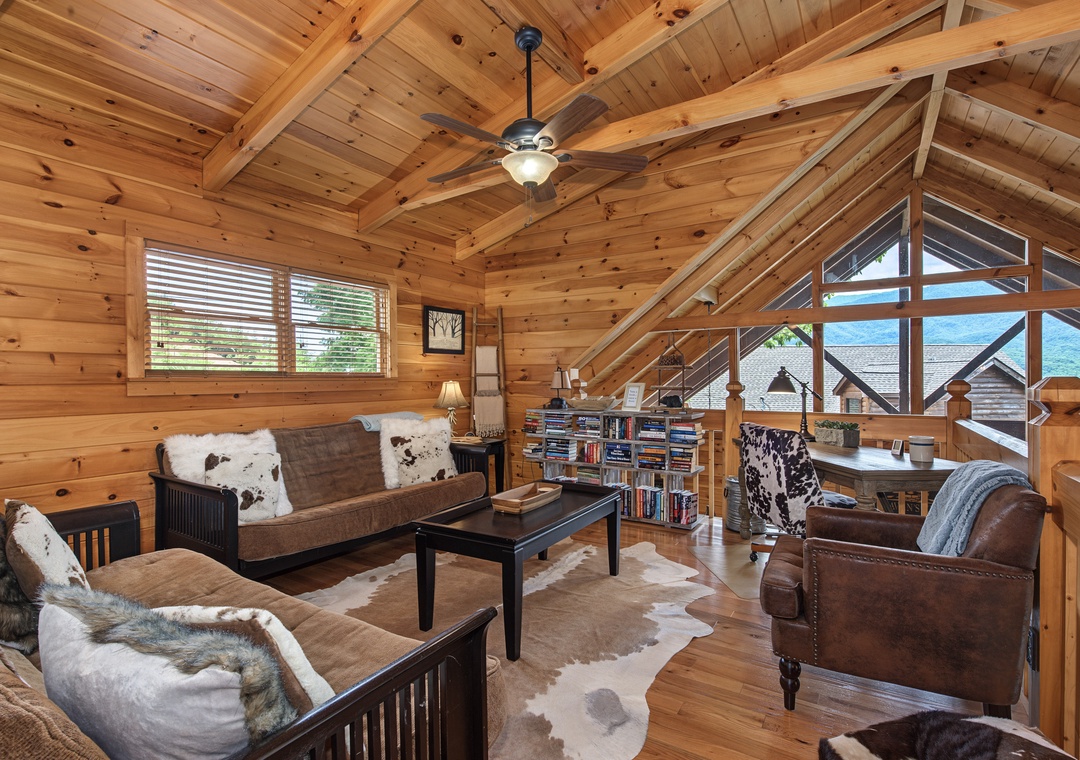 Unwind in this inviting loft lounge with vaulted wood-beamed ceilings, plush seating, and a cozy reading nook. Expansive windows frame stunning mountain views, while warm wood tones and rustic touches create your perfect retreat.