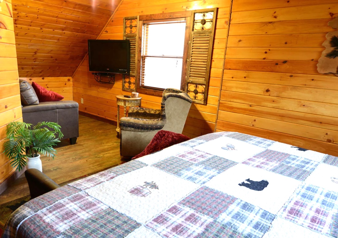 Unwind in your cozy log cabin bedroom with warm wood walls, comfortable seating, and rustic charm that makes you feel right at home.