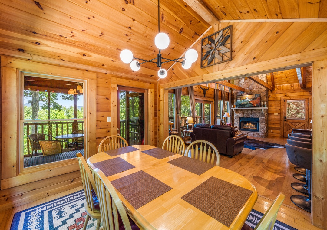 Gather around the dining table in this warm, wood-paneled cabin with stunning natural light and an open flow to the cozy living area and fireplace beyond.