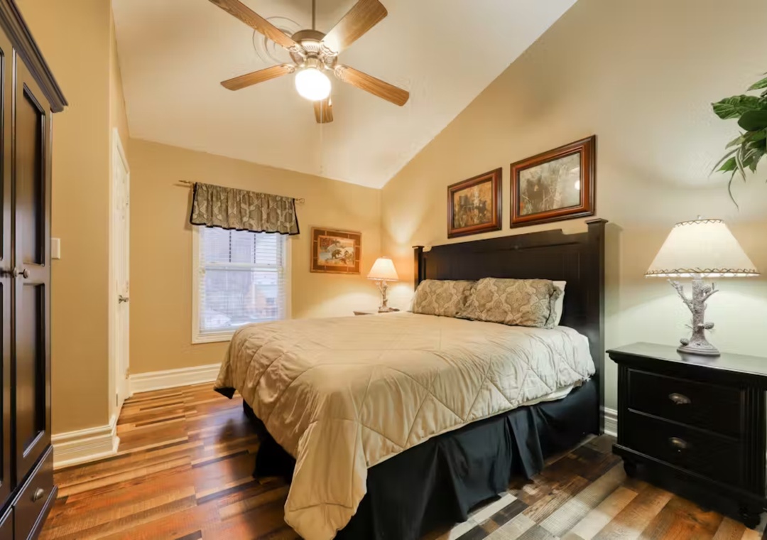 Your cozy bedroom features warm hardwood floors, elegant dark furniture, and a ceiling fan to keep you comfortable throughout your stay.