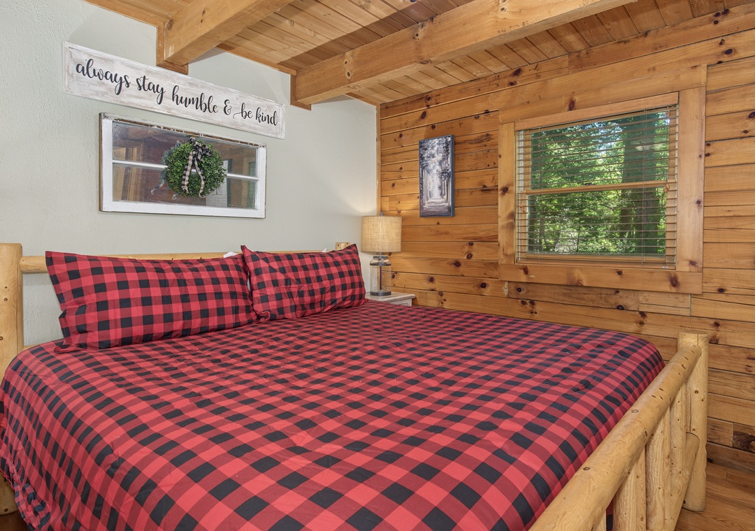 Sink into the soft plaid bedding and wake to natural light streaming through the window in this cozy wooden bedroom, where rustic charm meets comfort.
