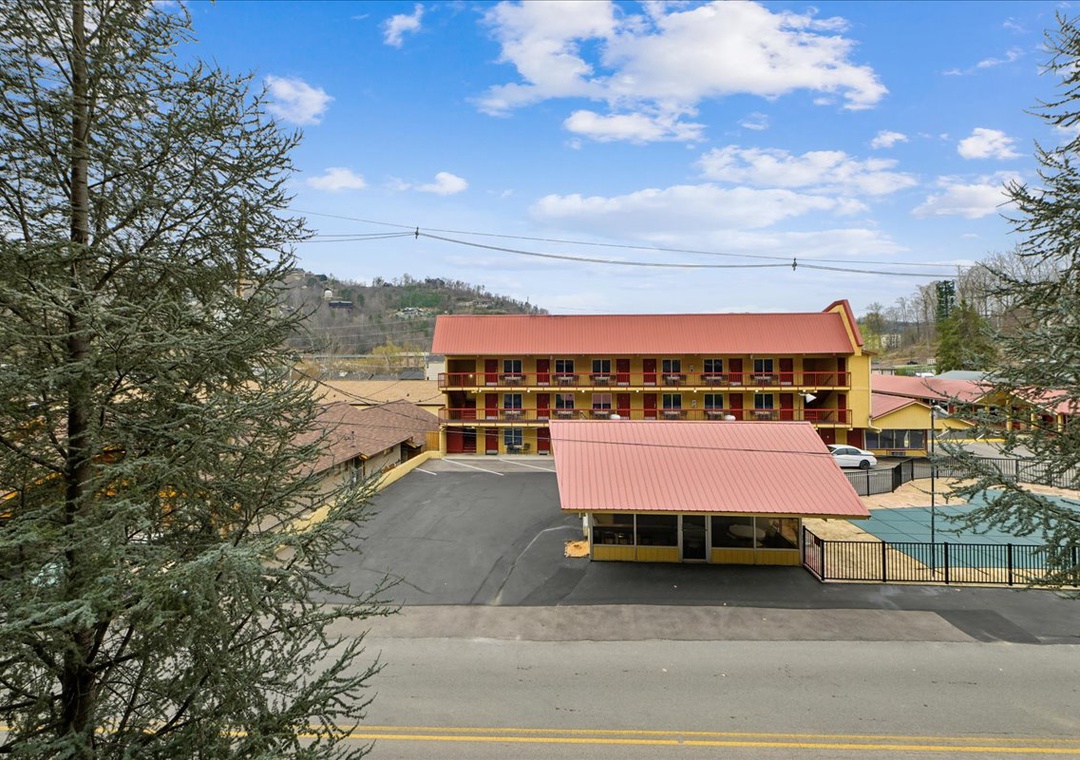 A charming mountain lodge with red roofing nestled among trees, featuring multiple levels and surrounded by rolling hills.