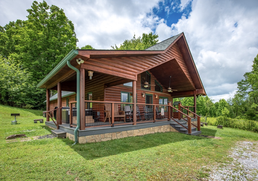 A rustic log cabin nestled in lush greenery offers a charming retreat with a spacious covered porch, perfect for enjoying the peaceful natural surroundings.