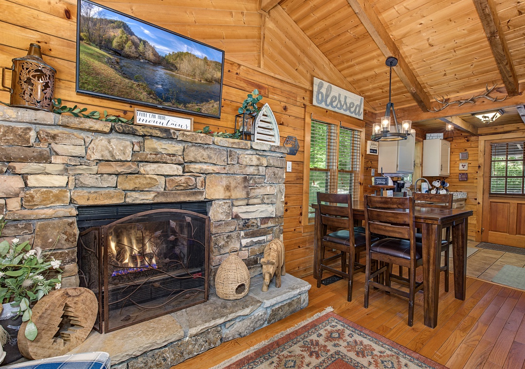 Gather around the stone fireplace for cozy evenings, or enjoy meals at your rustic high-top table—warm wood tones and vaulted ceilings make this cabin feel like home.