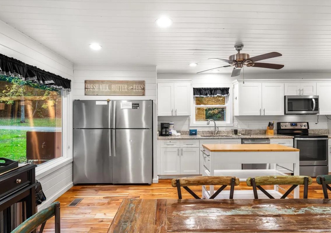 Bright farmhouse kitchen with stainless steel appliances and warm wood floors. Open layout perfect for cooking and gathering with loved ones around the rustic table.