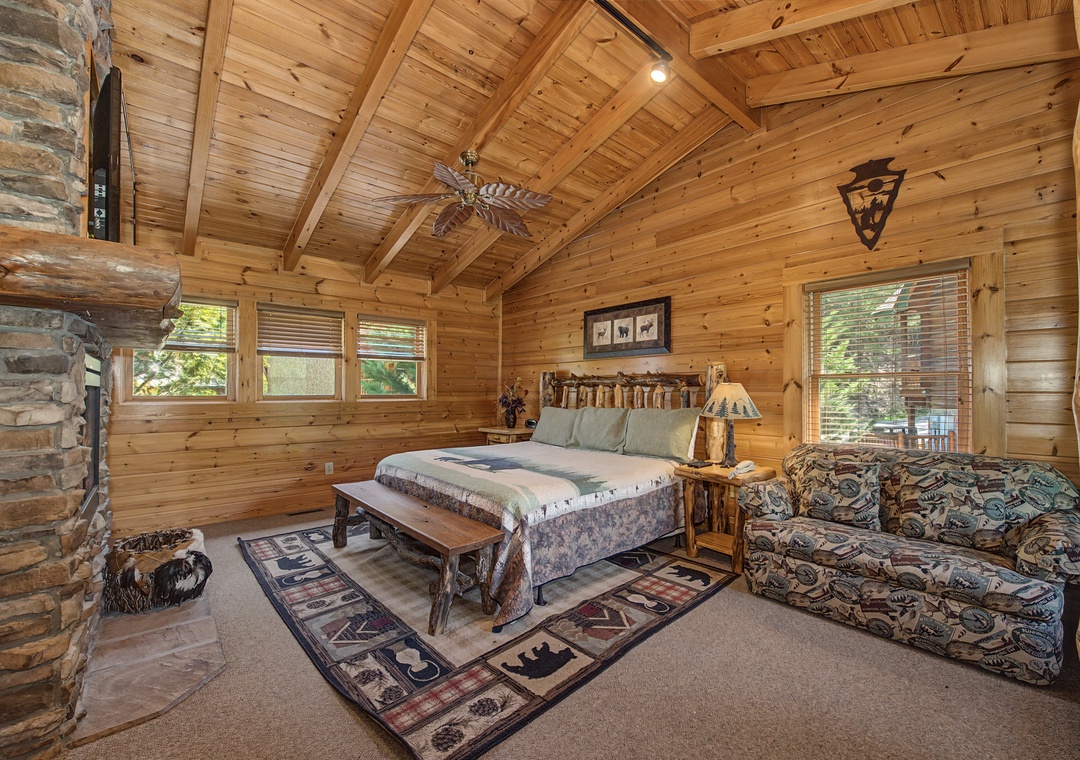 Unwind in this cozy log cabin bedroom with vaulted ceilings, stone fireplace, and rustic charm.