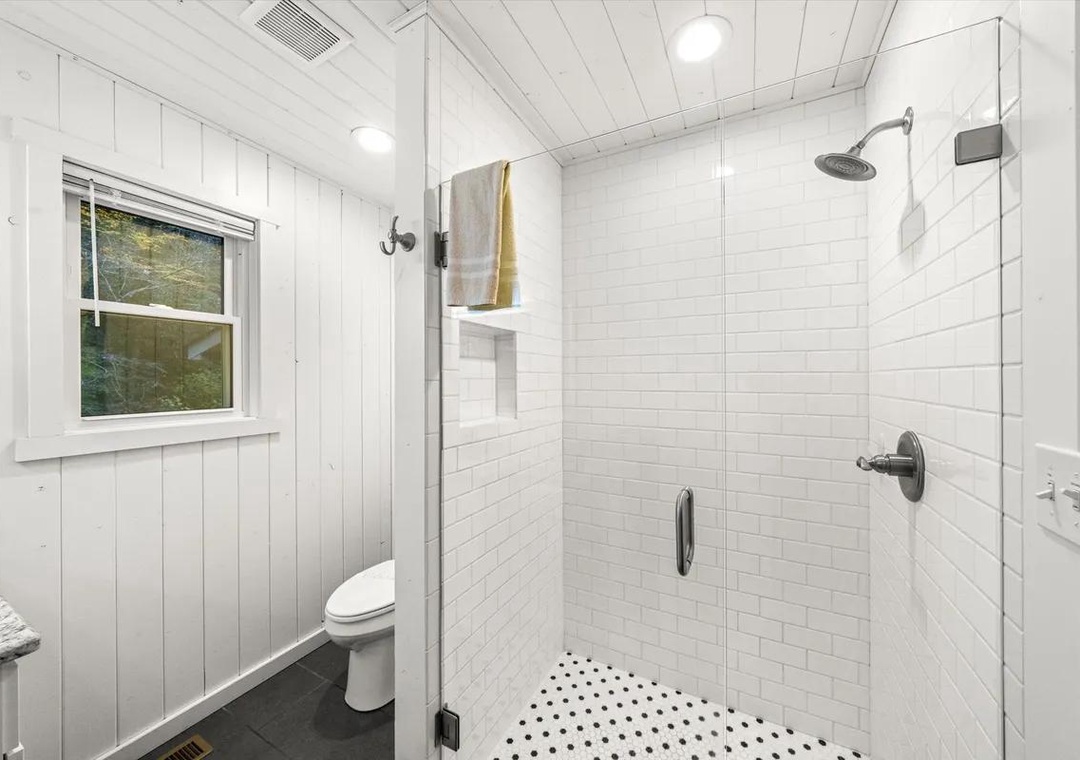 Step into your bright, modern bathroom featuring a spacious glass-enclosed shower with classic white tile and a cheerful window view. Everything you need for a refreshing start to your day awaits.