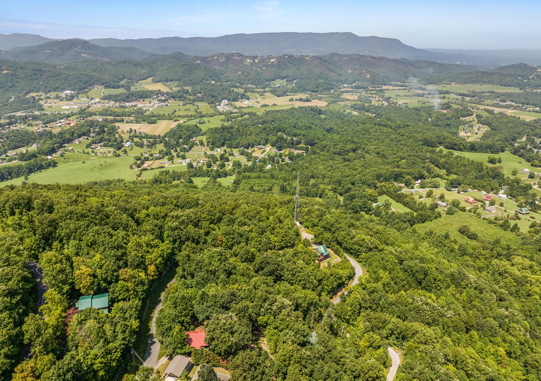 Aerial view showcasing the property's secluded mountain setting, surrounded by lush forests, rolling farmland, and distant peaks—a peaceful countryside escape.