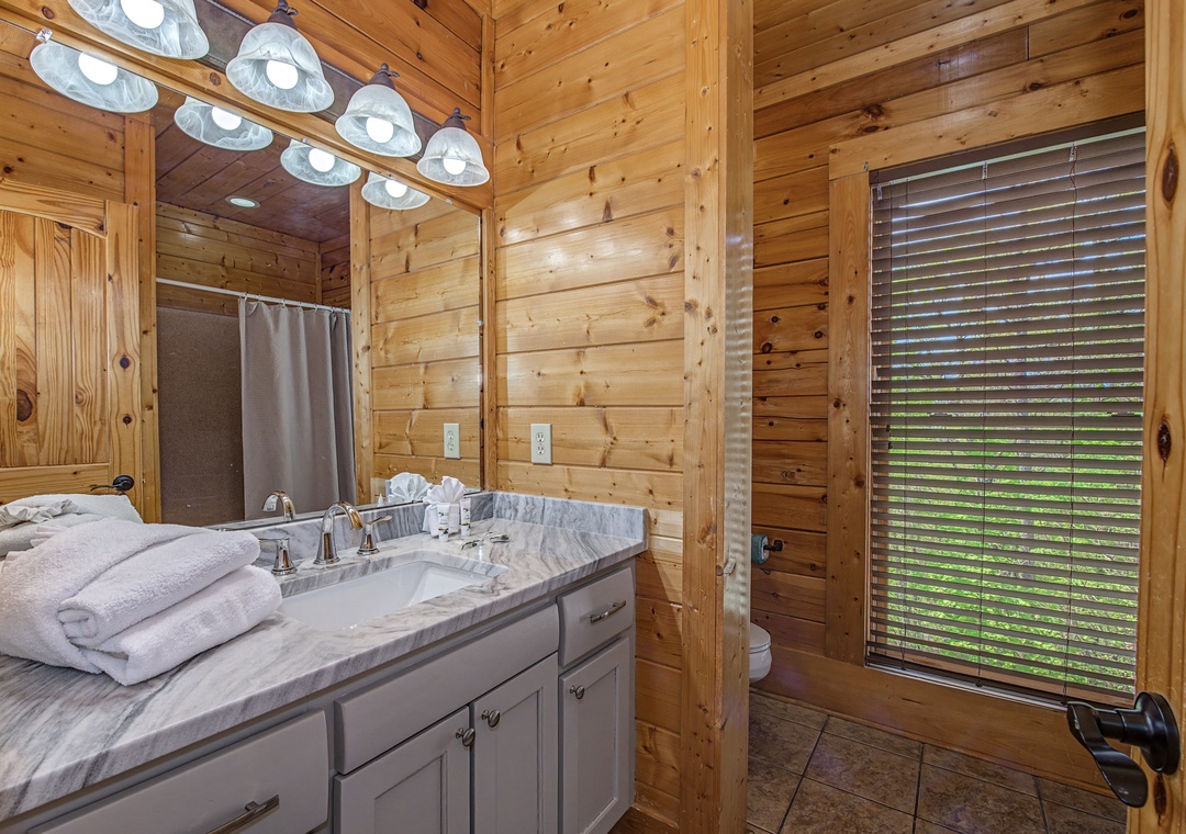 Unwind in your rustic-chic bathroom with marble countertops, cozy log walls, and elegant lighting creating the perfect mountain retreat atmosphere.