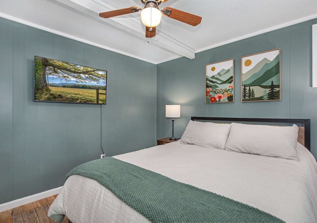 Unwind in this soothing bedroom featuring crisp linens, peaceful mountain artwork, and a ceiling fan for your comfort during restful nights.
