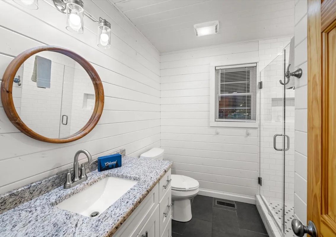 Step into your bright, farmhouse-style bathroom with shiplap walls, granite counters, and a walk-in glass shower designed for a refreshing start to your day.