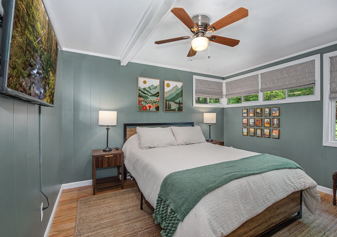 Settle into your serene retreat with soothing sage-green walls, crisp linens, and a cozy throw inviting restful nights under a gentle ceiling fan.