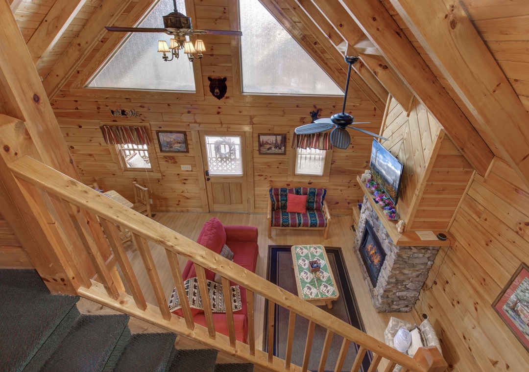 Stunning bird's-eye view of your cozy cabin living space, where soaring beams frame a stone fireplace and comfortable seating below.