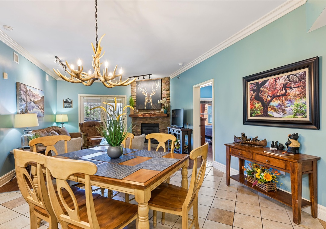 Your dining room features rustic charm with antler chandelier, stone fireplace, and warm wood furnishings creating the perfect gathering space.