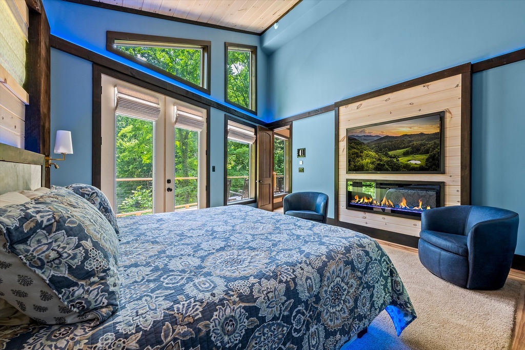 Sink into serenity in this stunning bedroom with soaring ceilings, expansive windows framing lush greenery, and a cozy fireplace. Your private balcony opens to nature's embrace, while plush seating invites peaceful relaxation.