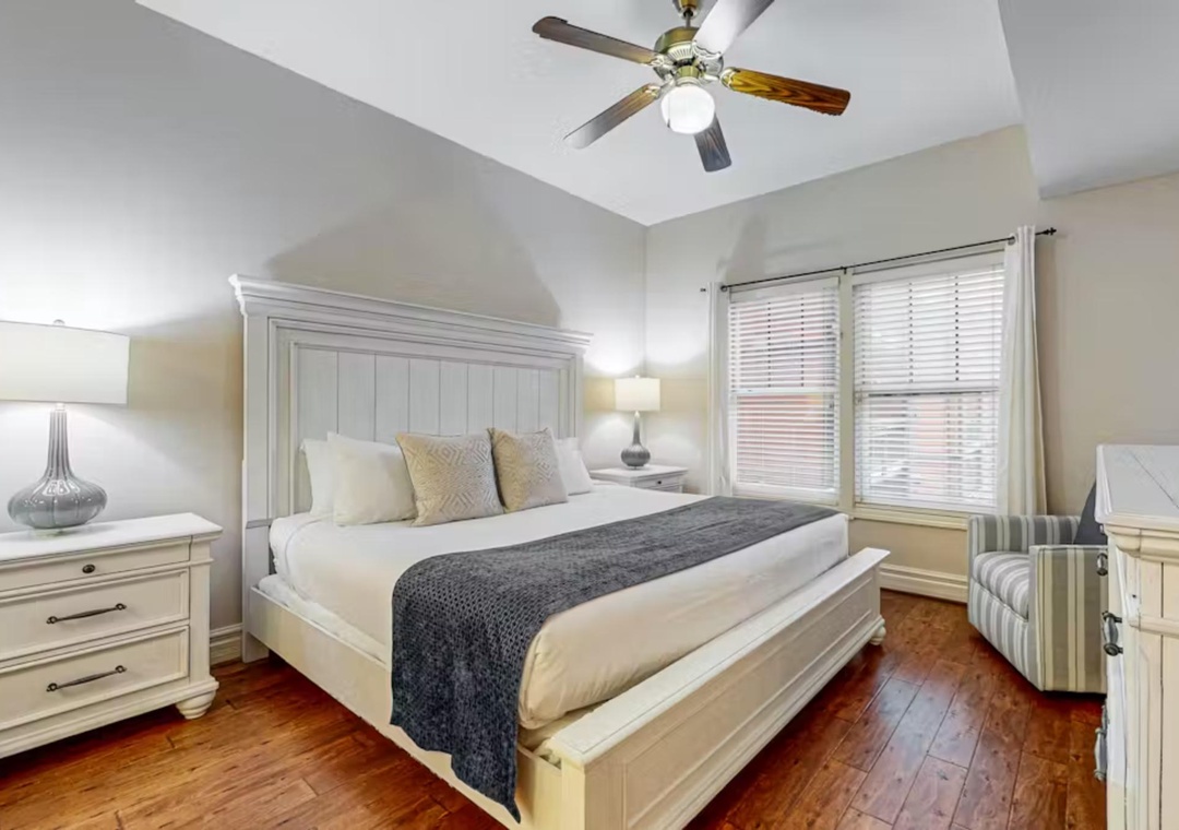 Unwind in your elegant bedroom featuring crisp white linens, warm hardwood floors, and gentle ceiling fan breezes for perfect comfort.
