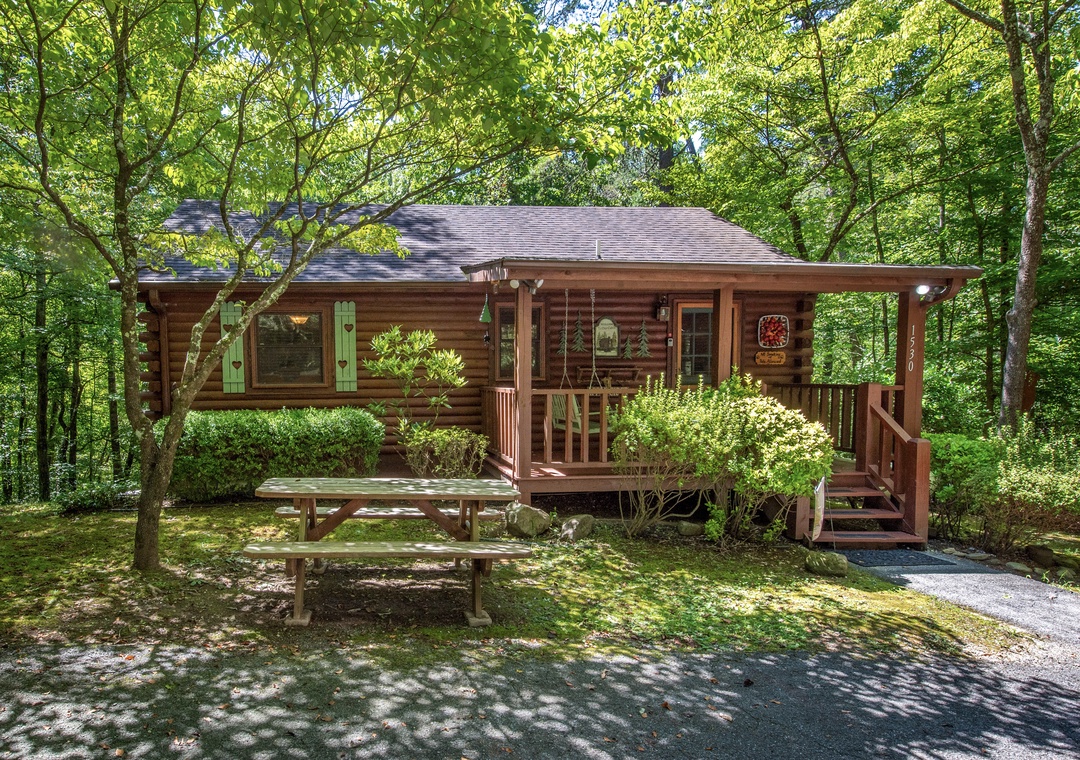 Charming log cabin tucked into lush forest surroundings, offering a peaceful woodland retreat with a welcoming front porch and tranquil natural setting.