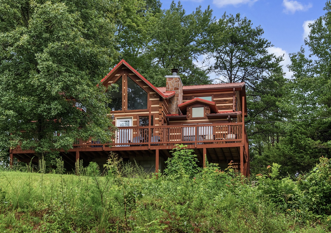 A charming log cabin retreat nestled among lush greenery, featuring a spacious deck and classic A-frame architecture perfect for a peaceful mountain escape.