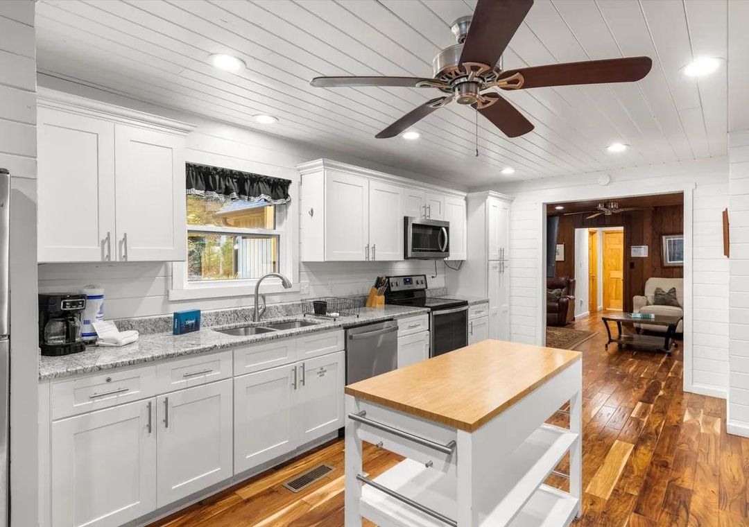 Your fully equipped kitchen invites home-cooked meals with granite counters, modern appliances, and a handy island workspace—all framed by bright white shiplap and warm wood floors.