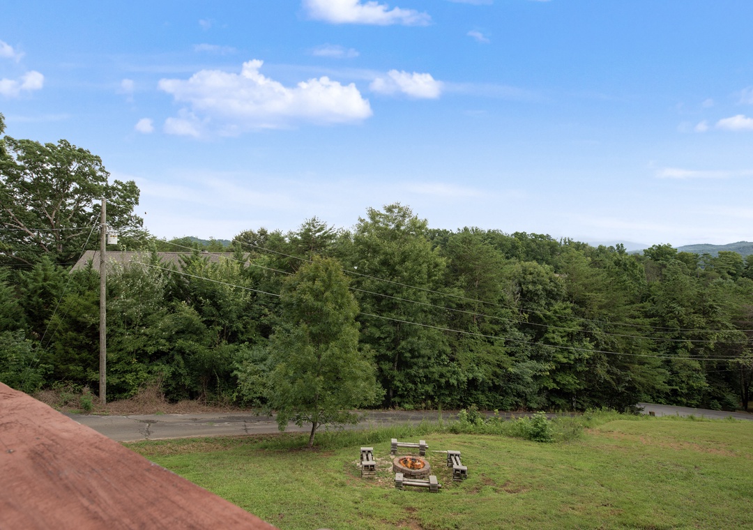 A spacious backyard with a fire pit and seating awaits your outdoor gatherings, framed by lush forest and distant mountain views under expansive skies.