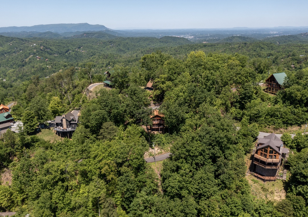 Aerial view of a mountain resort community surrounded by lush forests, with distant peaks and valleys stretching toward the horizon.