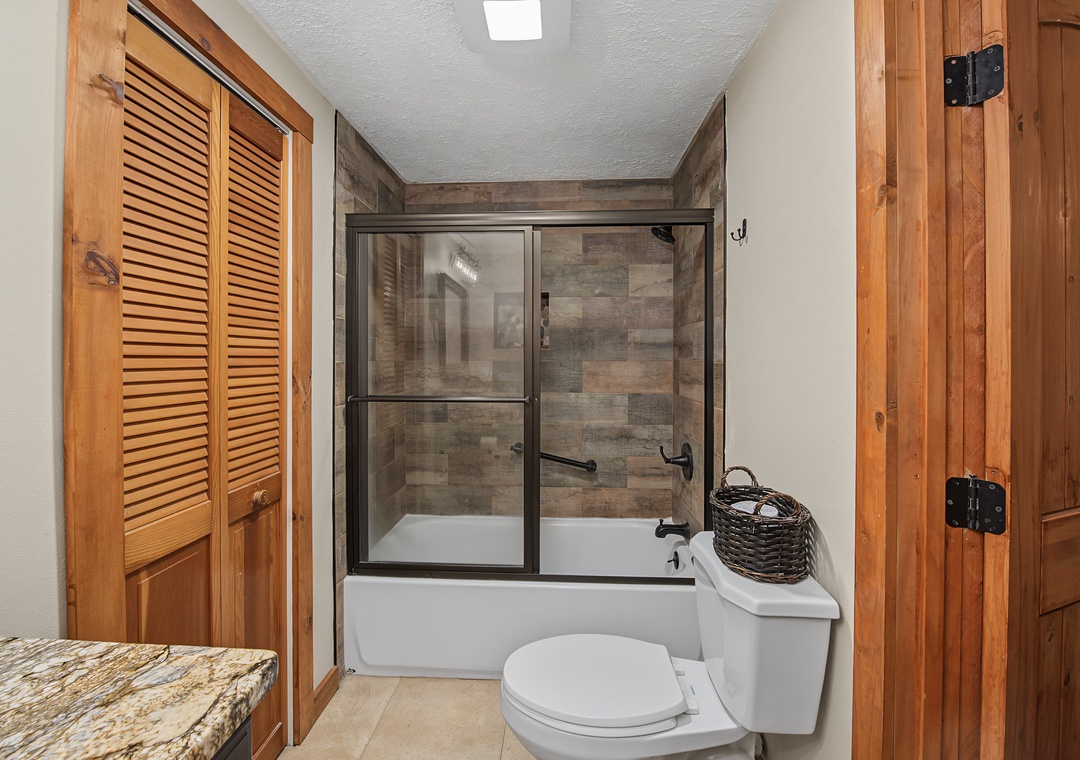 Step into your beautifully appointed bathroom, where wood-toned elegance meets modern comfort. The tiled tub and shower combo invites relaxation after a day of exploring.