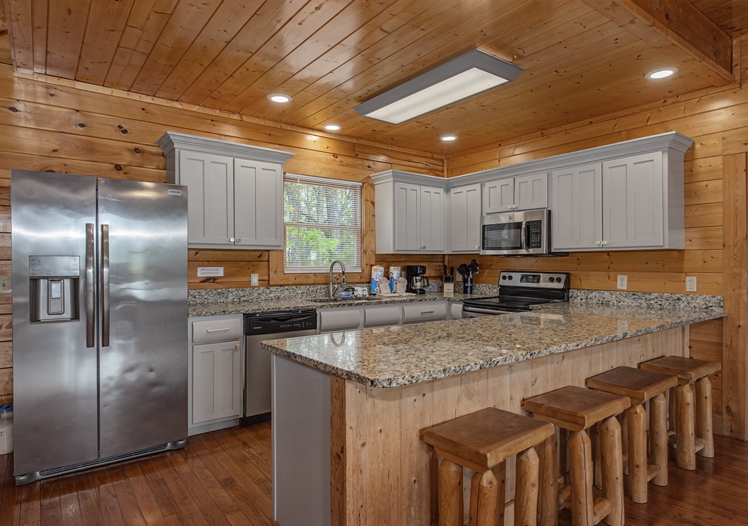 Your fully equipped kitchen features granite countertops, stainless steel appliances, and rustic log stools perfect for casual meals.