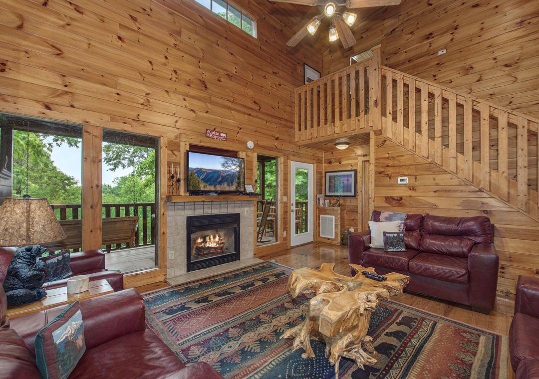 Unwind in your spacious, light-filled living room with soaring ceilings, a warm stone fireplace, and sweeping views of lush greenery through expansive windows that invite nature right in.