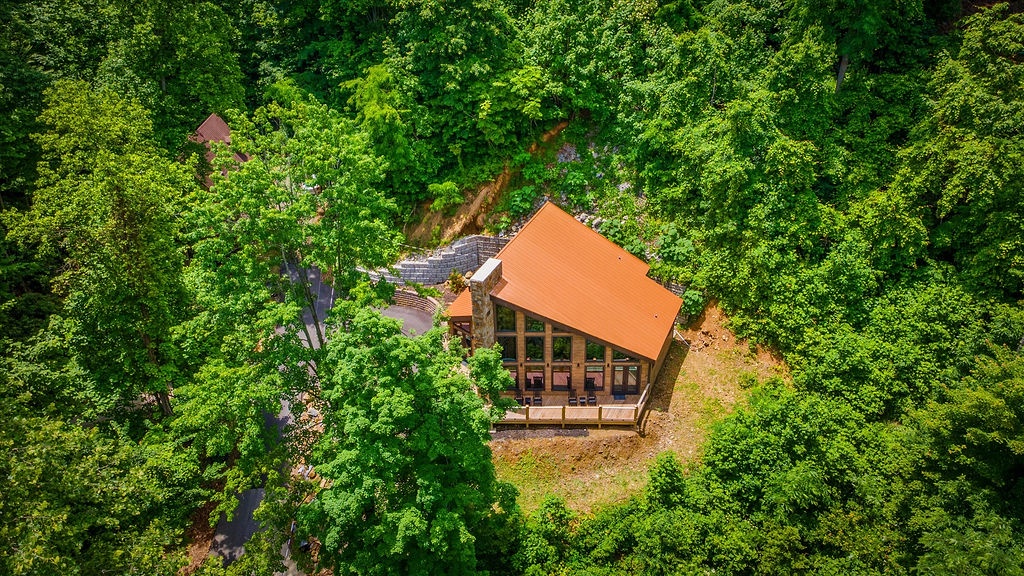Aerial view of a charming cabin retreat nestled privately among lush forest, featuring a distinctive orange roof and woodland surroundings perfect for a peaceful getaway.