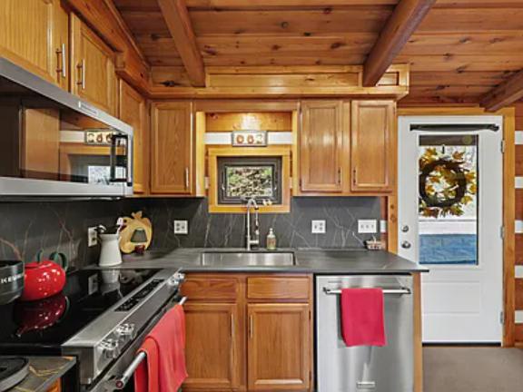 Step into a warm cabin-style kitchen with honey-toned cabinetry, stainless appliances, and charming wood-beamed ceilings that invite you to cook and gather in comfort.
