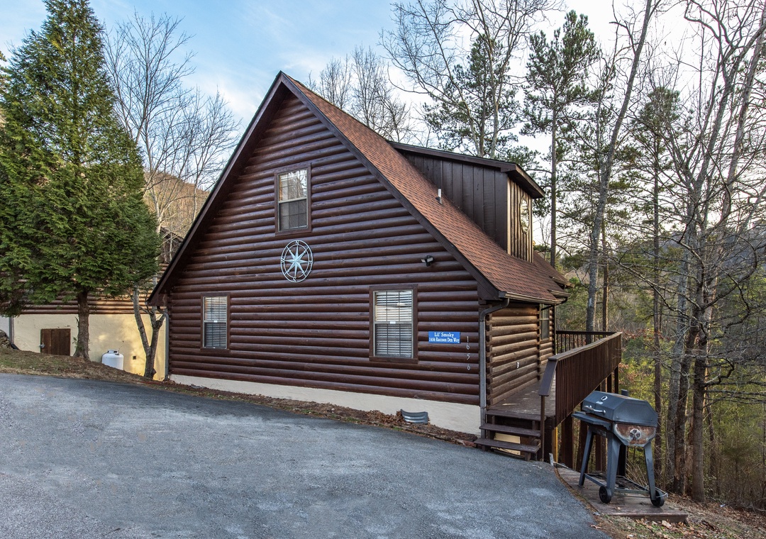 Charming log cabin nestled among towering trees, featuring convenient parking and outdoor grilling area for mountain getaway memories.