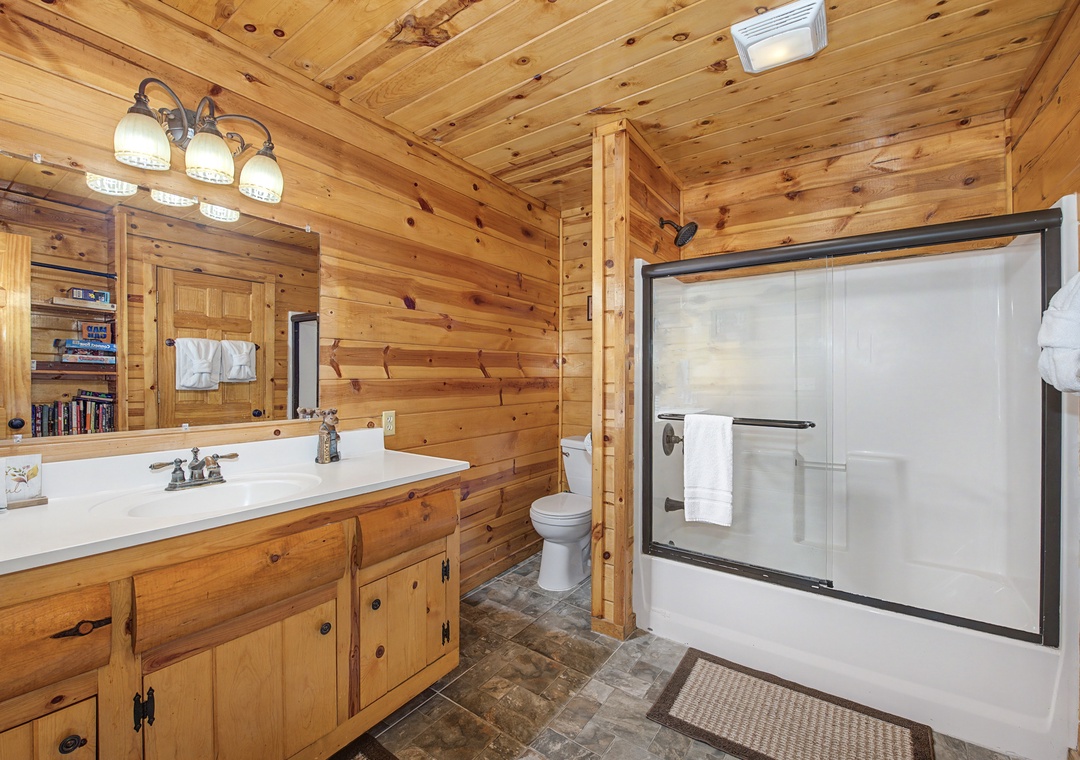 Your private bathroom features warm wood paneling, a spacious vanity, and a modern glass-enclosed tub-shower combo—perfect for unwinding after a day of adventure.