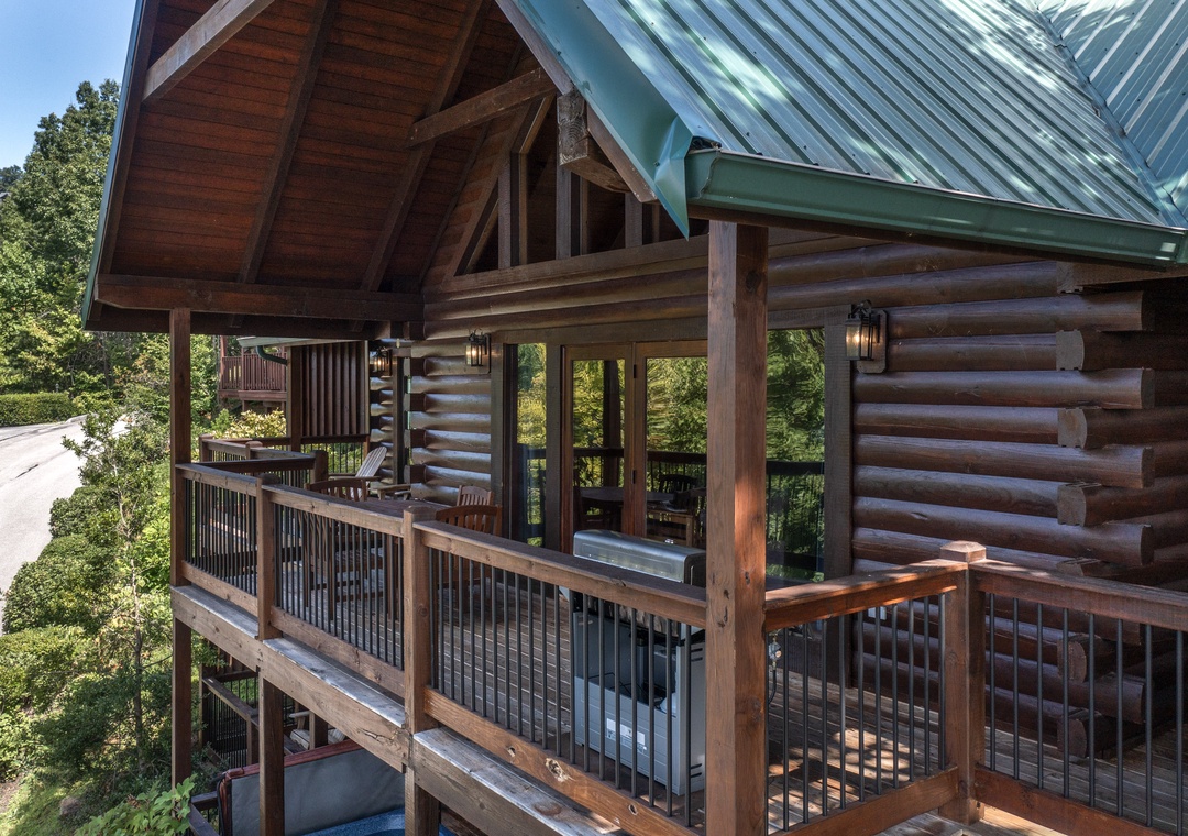 Rustic log cabin with wraparound deck surrounded by lush forest, featuring green metal roof and natural wood construction.
