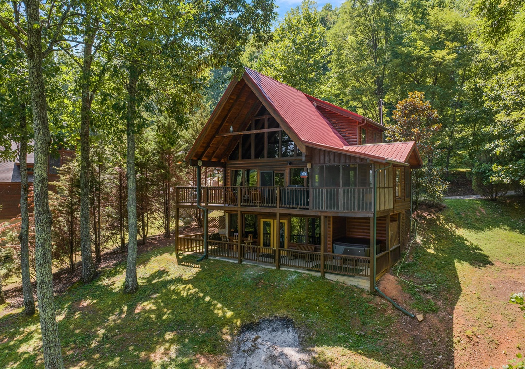 A charming A-frame cabin with a striking red metal roof nestled among towering trees, featuring wraparound decks and a private hot tub, offering a peaceful woodland retreat.