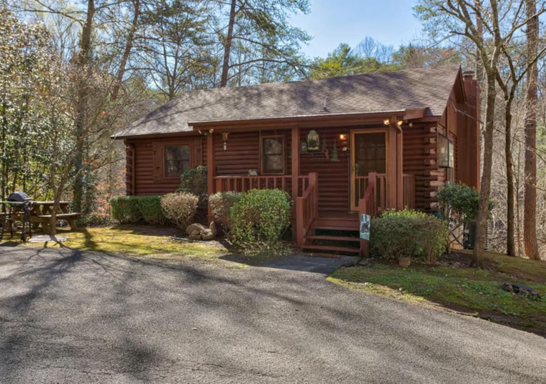 A cozy log cabin retreat nestled among towering trees, offering a peaceful escape in nature with convenient parking and outdoor seating just steps from your door.
