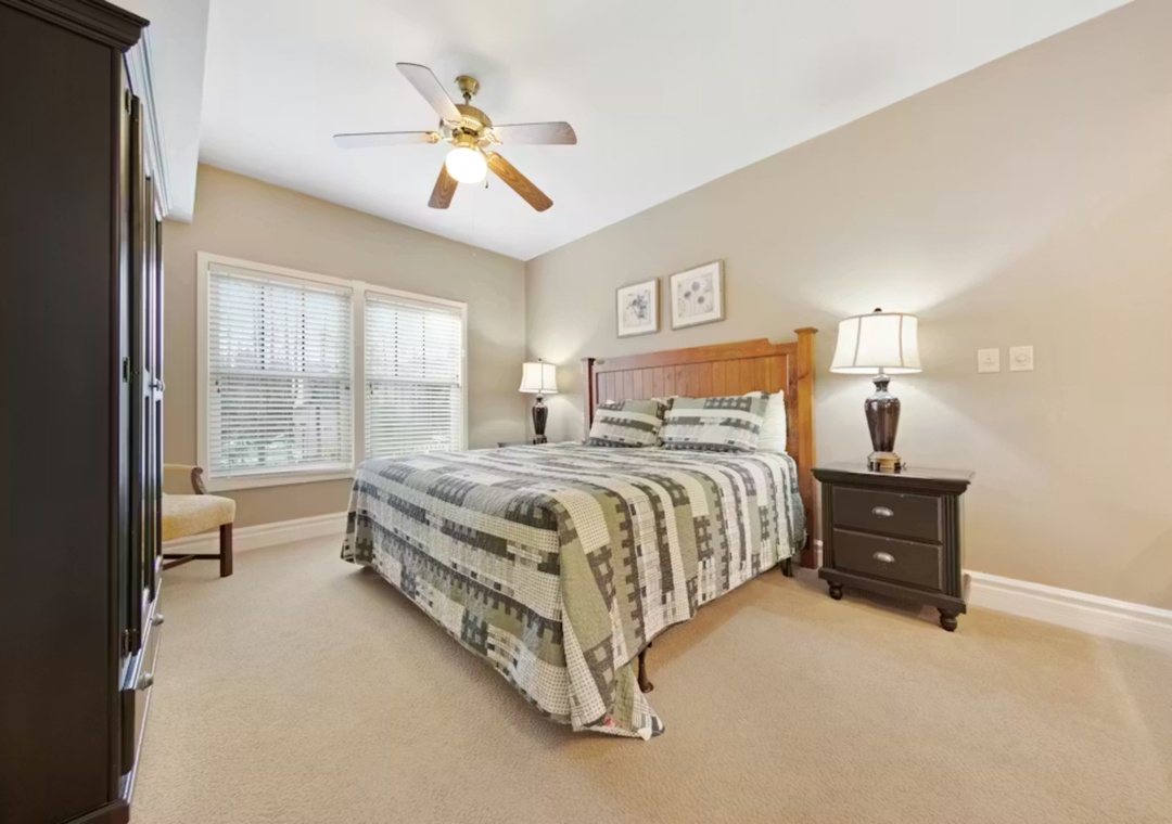 Drift off in this peaceful bedroom with its cozy quilt-topped bed, warm lighting, and gentle ceiling fan creating your perfect sleep sanctuary.