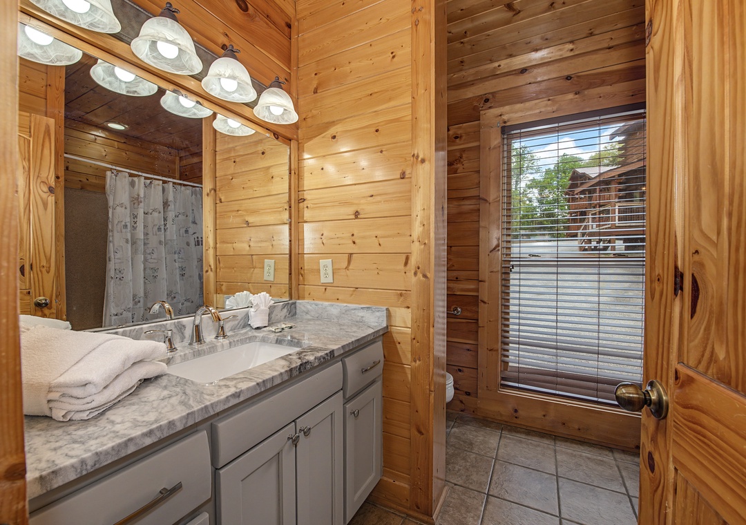 Freshen up in your rustic bathroom featuring elegant marble countertops, warm wood walls, and modern amenities for your comfort.