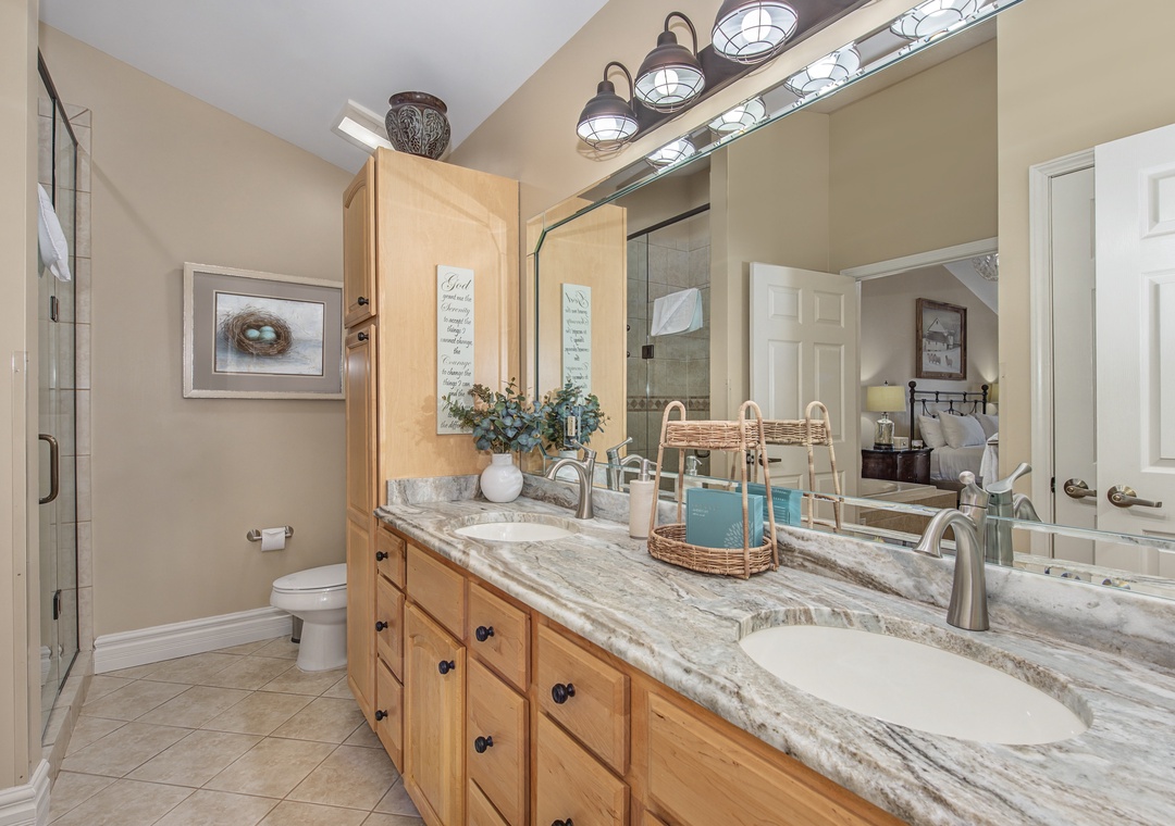 Enjoy your morning routine in this spacious bathroom featuring dual vanities, elegant marble countertops, and warm coastal lighting.