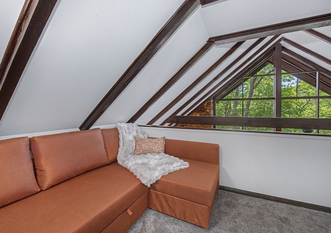 Nestle into this charming loft seating area where vaulted beams frame a stunning treetop view through the triangular window. Your perfect hideaway to unwind.