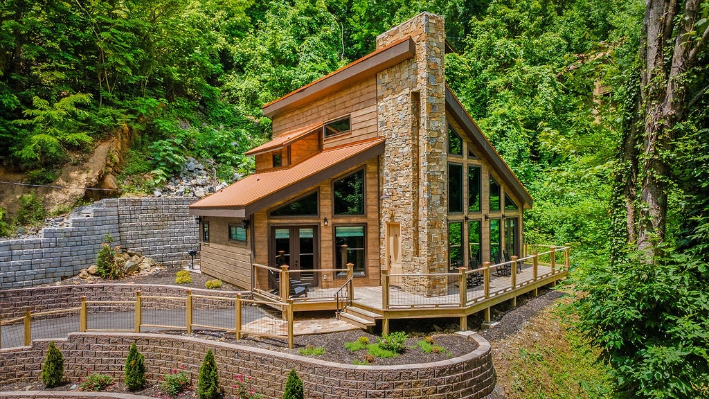 Modern wood cabin with stone chimney nestled in the forest, accessible via wooden walkways and landscaped terraces with privacy-enhancing retaining walls.