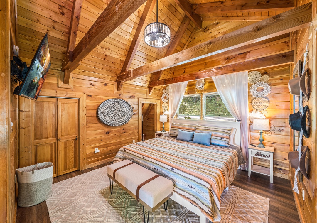 Drift off under soaring wooden beams and soft lighting. Your cozy bed awaits, framed by airy curtains and warm cabin charm—perfect for peaceful mountain nights.