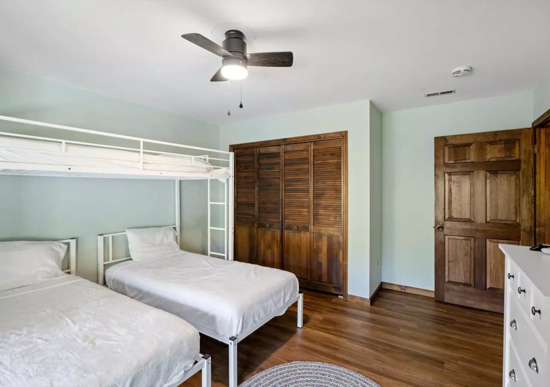 Sleep soundly in your spacious bedroom featuring fresh linens, wood floors, ceiling fan, and ample storage with charming rustic touches.